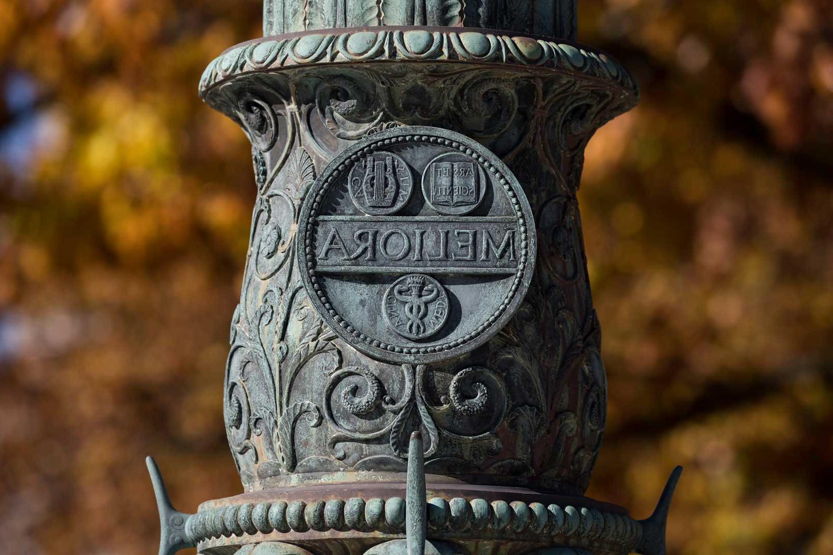Close-up of the Meliora seal inscription on flagpole on Eastman Quad at the University of Rochester